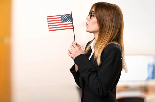 Joven mujer de negocios sosteniendo una bandera americana en la oficina sobre fondo desenfocado —  Fotos de Stock