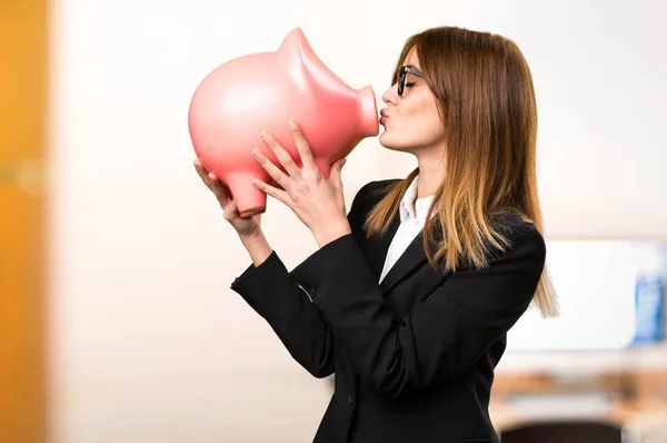 やり場のない背景のオフィスで、piggybank を保持している若いビジネス女性 — ストック写真