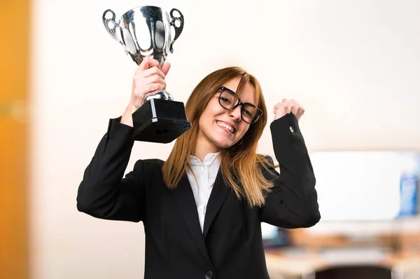 Jovem mulher de negócios segurando um troféu no escritório em fundo desfocado — Fotografia de Stock