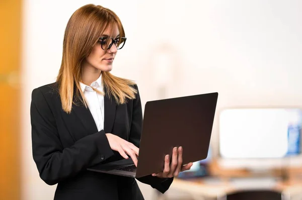 Joven mujer de negocios con portátil en la oficina en un fondo desenfocado —  Fotos de Stock