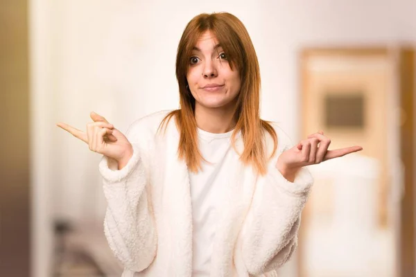 Jovem em roupão apontando para as laterais tendo dúvidas dentro de uma sala — Fotografia de Stock