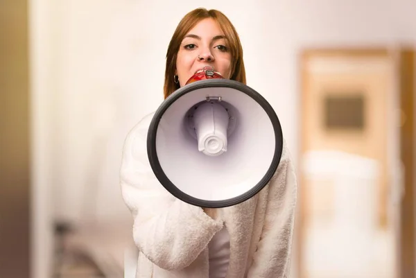 Jeune femme en robe de chambre tenant un mégaphone à l'intérieur d'une pièce — Photo