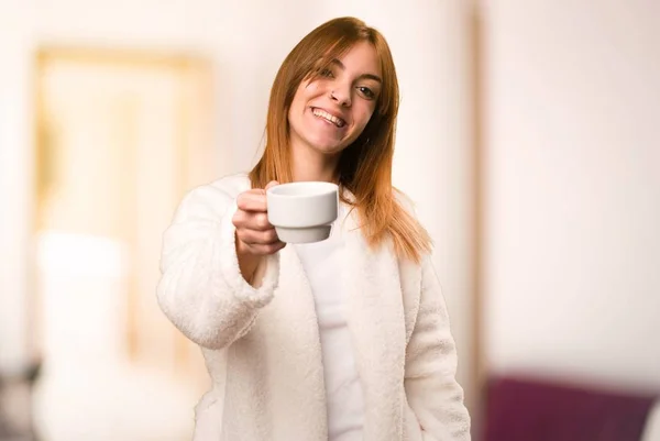 Молодая женщина в халате держит чашку кофе в комнате — стоковое фото