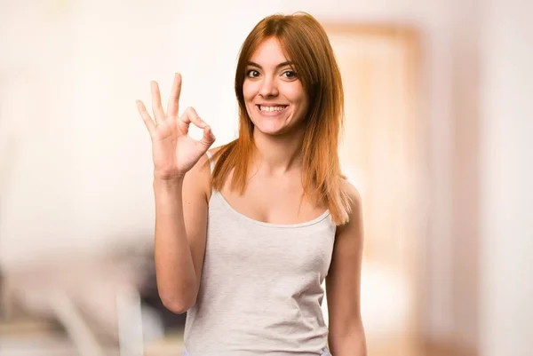 Beautiful girl in pajamas making OK sign inside a room — Stock Photo, Image