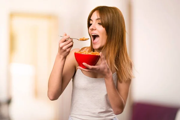 Menina bonita em pijama comendo cereais de uma tigela dentro de uma sala — Fotografia de Stock