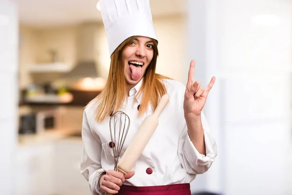Beautiful chef woman making horn gesture in the kitchen