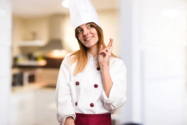 Beautiful chef woman with her fingers crossing in the kitchen