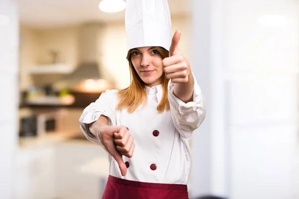 Beautiful chef woman making good-bad sign in the kitchen