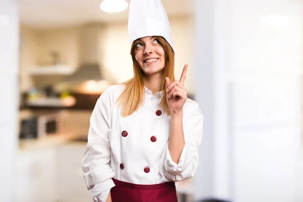 Beautiful chef woman pointing up in the kitchen