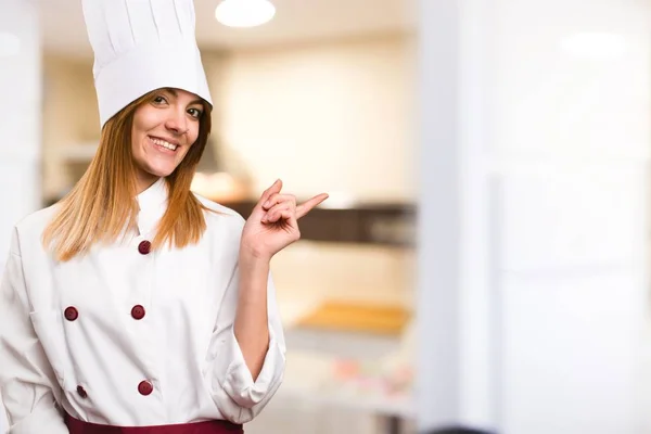 Красивая женщина-повар указывает на боковую сторону на кухне — стоковое фото
