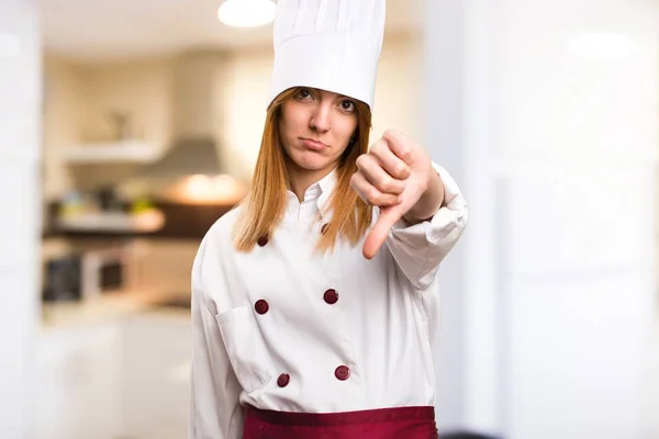 Beautiful chef woman making bad signal in the kitchen