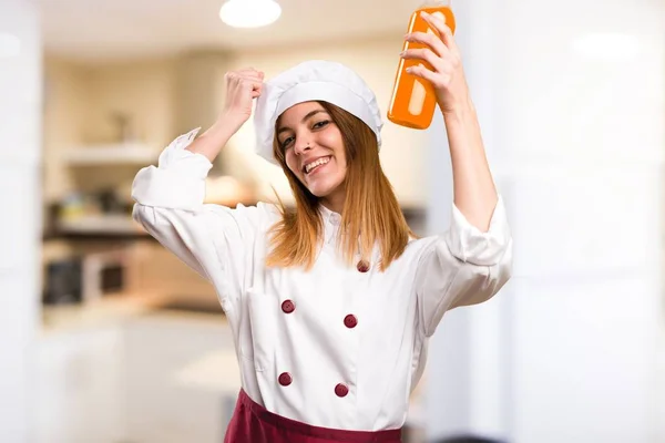 Joyeux beau chef femme tenant un jus d'orange dans la cuisine — Photo
