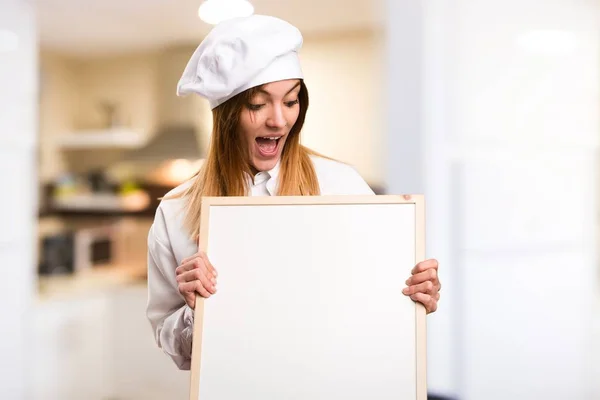 Sorprendido Hermosa chef mujer sosteniendo un cartel vacío en la cocina — Foto de Stock