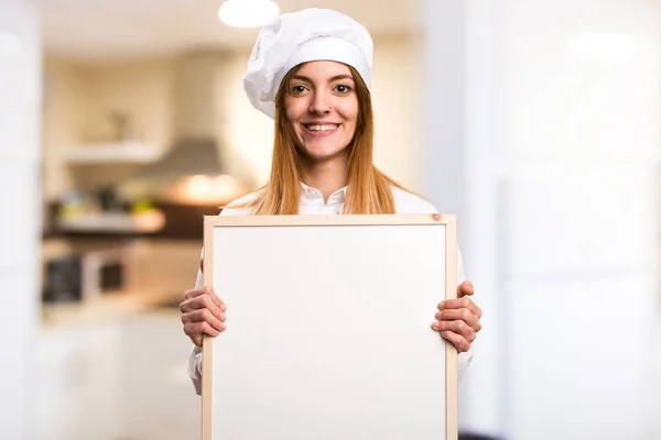 Happy Beautiful chef woman holding an empty placard in the kitchen