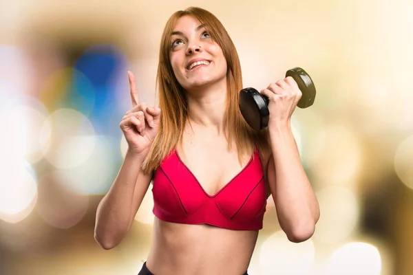 Bella donna sportiva con manubri che puntano su sfondo sfocato — Foto Stock