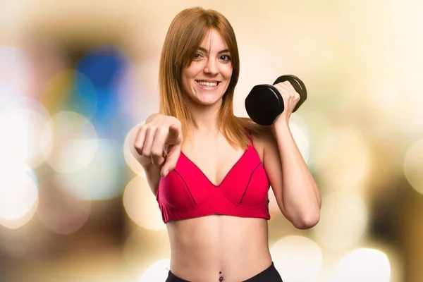 Hermosa mujer deportiva con mancuernas apuntando al frente sobre un fondo desenfocado — Foto de Stock