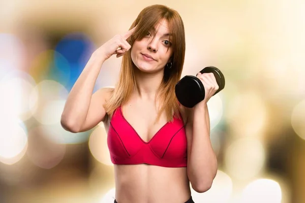 Hermosa mujer deportiva con mancuernas pensando en fondo desenfocado — Foto de Stock