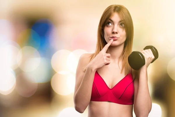 Hermosa mujer deportiva con mancuernas pensando en fondo desenfocado — Foto de Stock