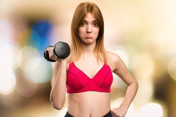 Sad beautiful sport woman with dumbbells on unfocused background