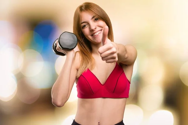 Hermosa mujer deportiva con mancuernas con el pulgar hacia arriba en el fondo desenfocado — Foto de Stock