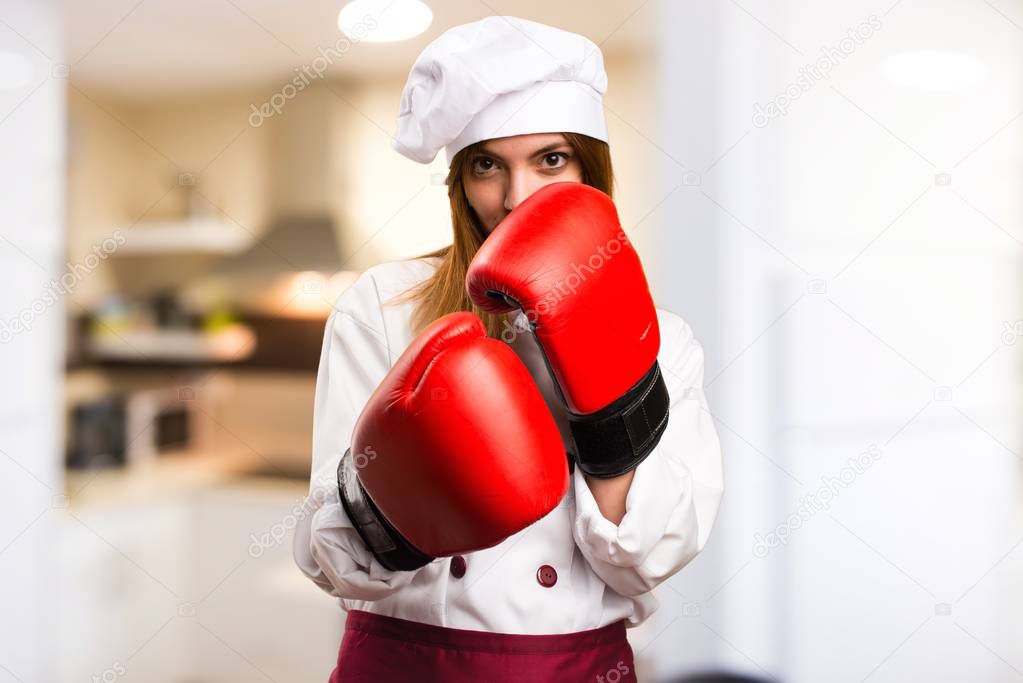 Beautiful chef woman with boxing gloves in the kitchen