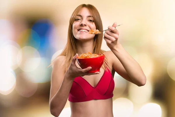 Young sport woman eating cereals from a bowl on unfocused background — Stock Photo, Image