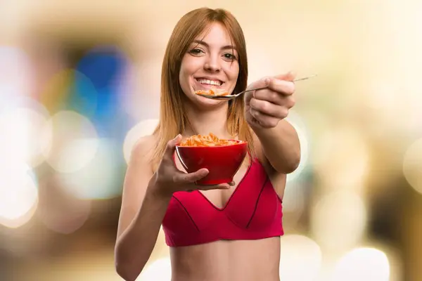 Jovem mulher do esporte comendo cereais de uma tigela em fundo desfocado — Fotografia de Stock