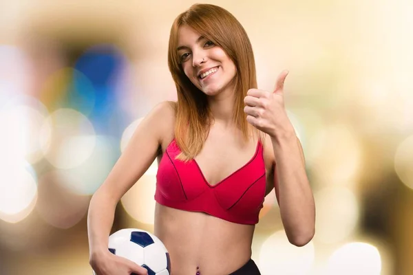 Junge Sportlerin hält vor unkonzentriertem Hintergrund einen Fußball in der Hand — Stockfoto