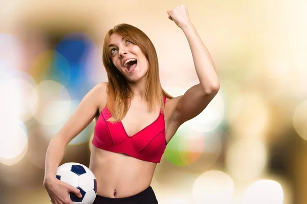 Joven deportista sosteniendo una pelota de fútbol sobre fondo desenfocado — Foto de Stock