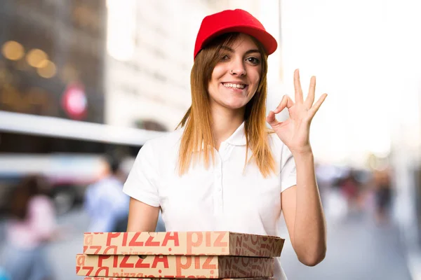 Pizza delivery woman making OK sign  on unfocused background