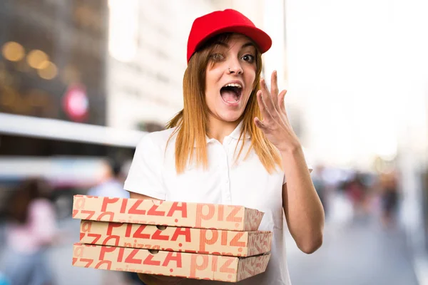 Mulher de entrega de pizza fazendo gesto surpresa em backg desfocado — Fotografia de Stock