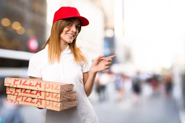 Mujer entregadora de pizza apuntando hacia el lateral en la espalda desenfocada — Foto de Stock