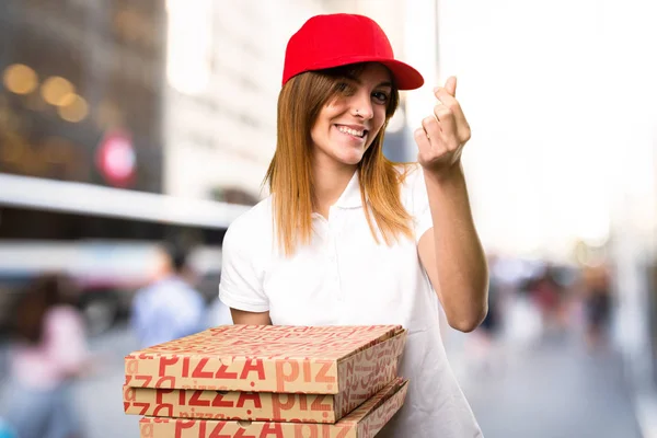 Pizza delivery woman making money gesture  on unfocused backgrou