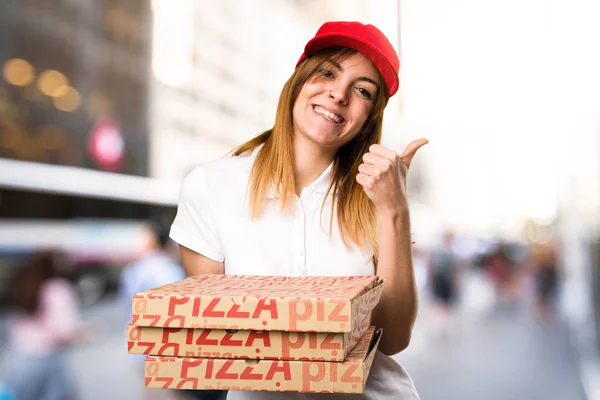 Kobieta dostawy pizzy z kciuk na nieostre tło — Zdjęcie stockowe