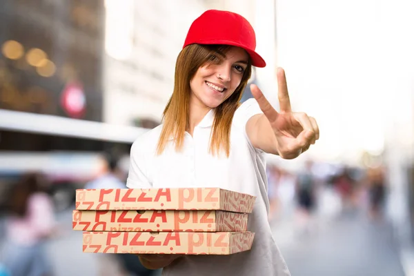 Pizza delivery woman making victory gesture  on unfocused backgr