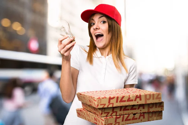 Доставка пиццы женщина держит лампочку на несосредоточенном фоне — стоковое фото