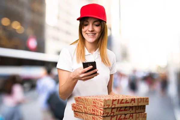 Pizza levering vrouw praten tot mobiele op ongericht achtergrond — Stockfoto