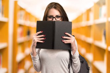 Kitaplığa bir kitapta arkasına saklanmış öğrenci kadın