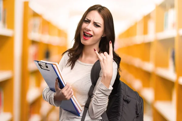 Studerande kvinna gör horn gest i ett bibliotek — Stockfoto