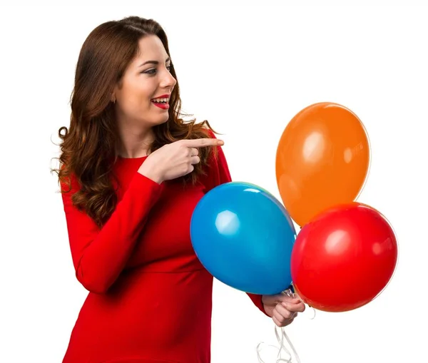 Hermosa joven sosteniendo globos y apuntando hacia el lateral — Foto de Stock