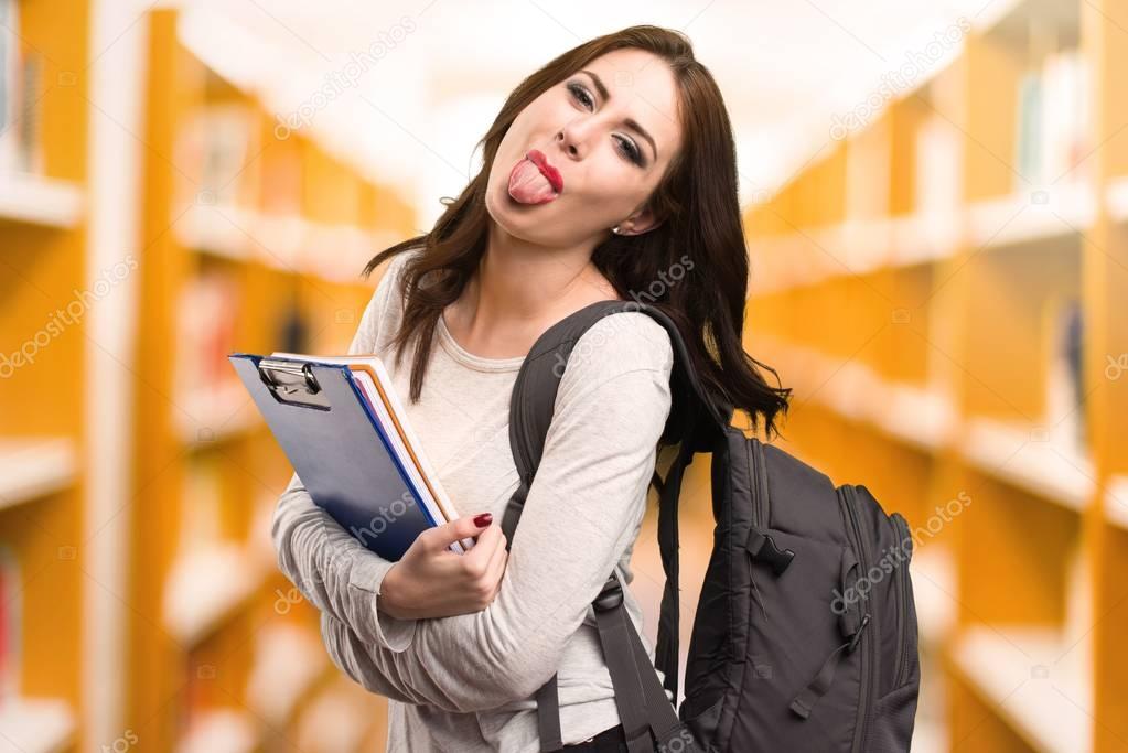 Student woman taking out her tongue in a library