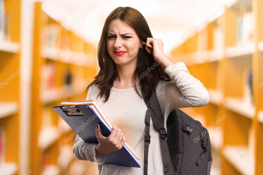 Student woman covering her ears in a library