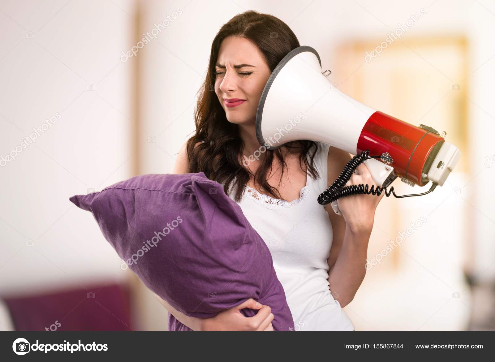 Beautiful young girl with a pillow holding a megaphone in her apartment