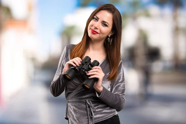 Vacker ung flicka med kikare på ofokuserat bakgrund — Stockfoto
