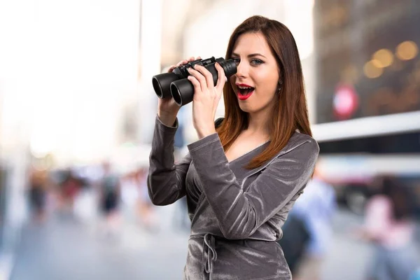 Vacker ung flicka med kikare på ofokuserat bakgrund — Stockfoto