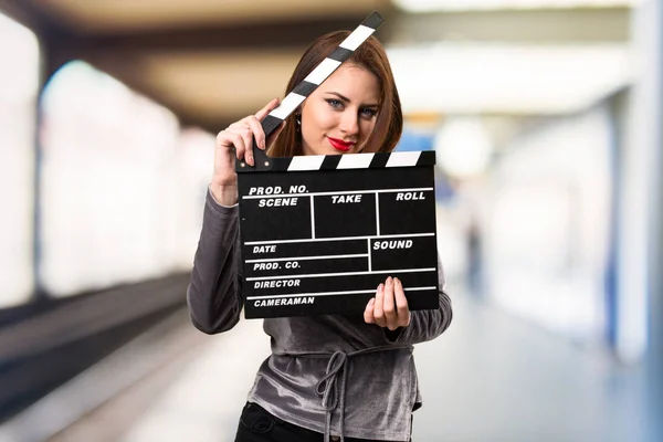 Beautiful young girl holding a clapperboard on unfocused backgro — Stock Photo, Image