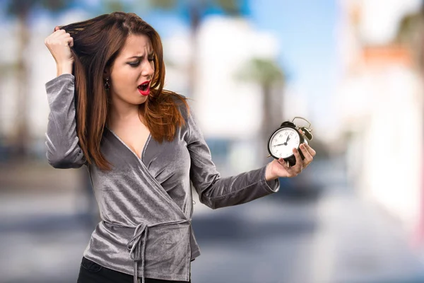 Beautiful young girl holding vintage clock on unfocused backgrou — Stock Photo, Image