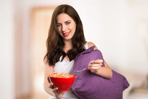Bella ragazza con un cuscino che tiene una ciotola di cereali nel suo appartamento — Foto Stock