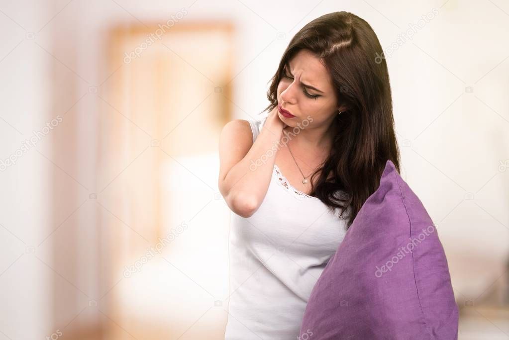 Beautiful young girl with a pillow with neck pain in her apartment