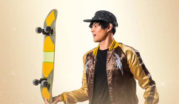 Asiático urbano hombre con skate en ocre fondo — Foto de Stock